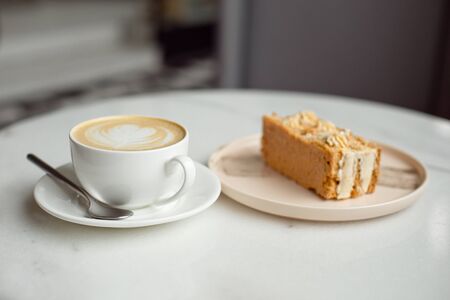 Slice of caramel cake and a fork on the right side. A cup of hot coffee with ground in the background.Close-up.の写真素材