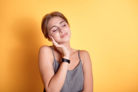 Portrait of a young beautiful girl in a gray T-shirt on thin britain, a happy blonde model smiling with a snow-white smile on a yellow wall.の写真素材