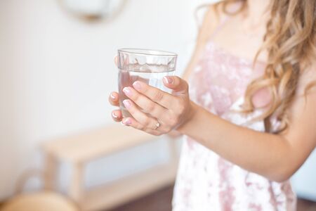 Female hands holding a clear glass of water. Slime body on background. Healthy lifestyleの写真素材