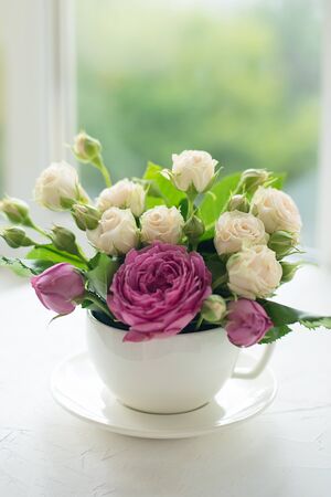 A bouquet of white roses in a cup on a white table opposite the window.の写真素材