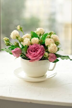 A bouquet of white roses in a cup on a white table opposite the window.の写真素材