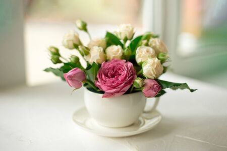 A bouquet of white roses in a cup on a white table opposite the window.の写真素材