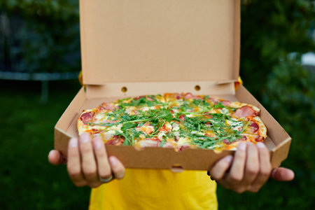 Pizza delivery man,Unrecognizable male, courier delivering pizza in park, open box. Fast Food delivery service conceptの写真素材