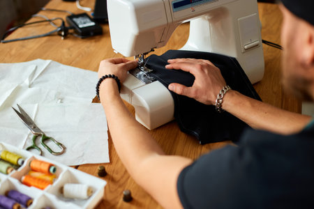 Man sews clothes on sewing machine,  male tailor working with sewing in atelier, textile industry,...