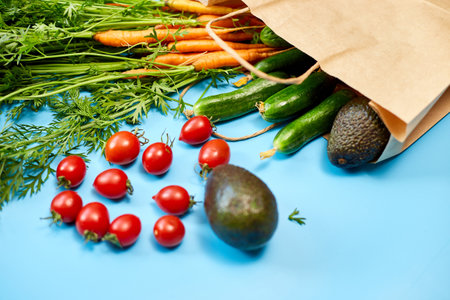 Flat lay vegetables, carrots, cucumbers, avocados, tomatoes in a paper bag for shopping on the blue...
