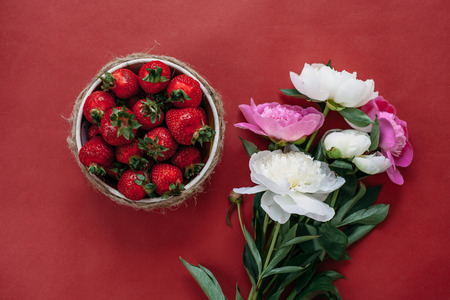 Ripe strawberries in a heart carved into the wood with pink peonies on the old wooden background. Place for text. Top view.の写真素材