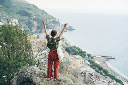 A cute teenage girl stands along a handrail overlooking the Mediterranean Sea and hillside villas in the fishing village turned tourism destination of Positano, Italy.の写真素材