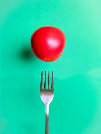 Levitating tomato over a fork on a turquoise background. Healthy eating concept. Cooking template.の写真素材