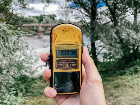 Dosimeter in a hand with the inscription mode and threshold, and described different modes of operation, gamma dose rate, gamma dose, real time, alarm clock, against the background of a Pripyat river.の写真素材