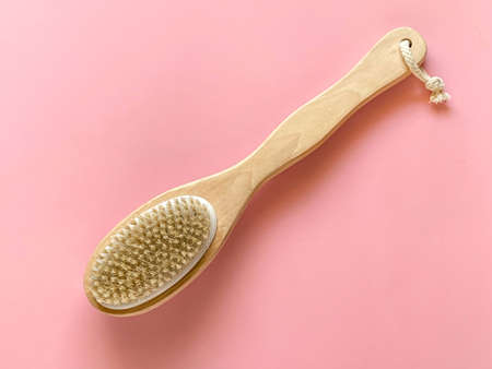 Brush for dry anti-cellulite massage or brushing in the hand of a girl in soft pink colors. Beauty...