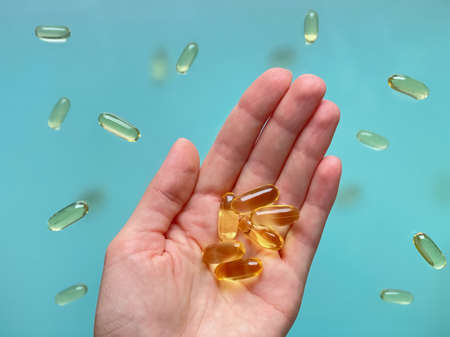 A woman's hand holds several omega 3 capsules against the background of omega 3 capsules levitating...