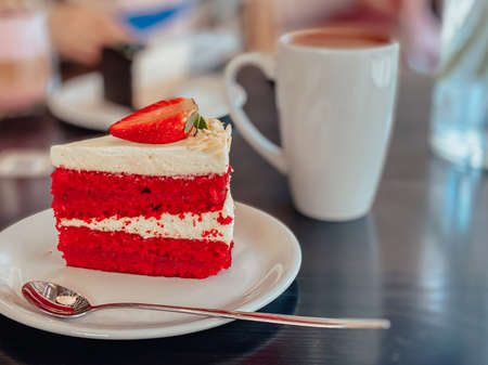 Piece of cake in white and red colors with sponge cake, cream and decoration on top of the cake in the form of strawberry on the table in the restaurant.の写真素材
