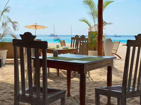 Restaurant tables against the backdrop of the ocean, ships, palm trees and beautiful white sand. Beach vacation and travel concept.の写真素材