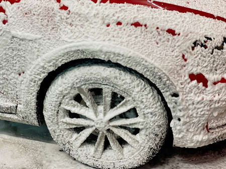 Front right wheel of a red car on which foam is applied to wash a car at a self-service car wash.の写真素材