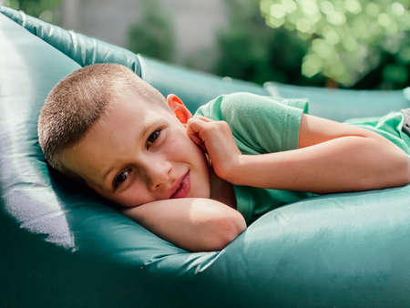 Portrait of a caucasian boy 7 years old in a green t-shirt resting on a lamzak, inflatable lounger.