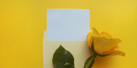 Yellow envelope with a white mockup sheet and yellow rose next to it on color of the year 2021 illuminating background.の写真素材