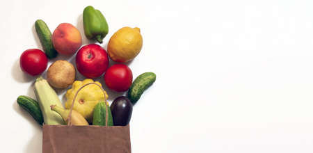 A paper shopping bag with vegetables and fruits, tomato, cucumber, squash, pepper, lemon, eggplant, zucchini, banana, apple, peach on white backgroundの写真素材