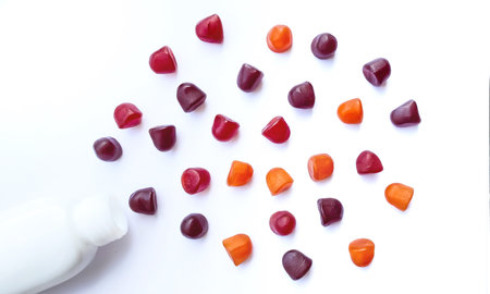 Group of red, orange and purple multivitamin gummies with the bottle isolated on white background.の写真素材