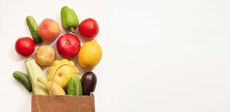 A paper shopping bag with vegetables and fruits, tomato, cucumber, squash, pepper, lemon, eggplant, zucchini, banana, apple, peach on white backgroundの写真素材