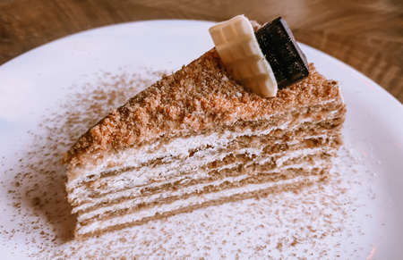 Close-up on a table in a restaurant in a white plate a piece of honey cake decorated with white and...