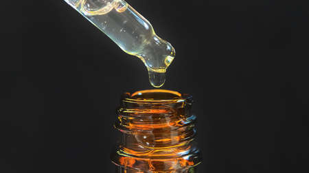 Pipette with a drop of face serum or oil for the face and hyaluronic acid on beautiful black background, close-up.の写真素材