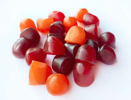 Close-up texture of red, orange and purple multivitamin gummies on white background. Healthy...