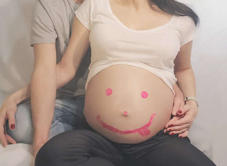 Caucasian pregnant woman and a man who hugs her waist and balloons and a toy bear near them