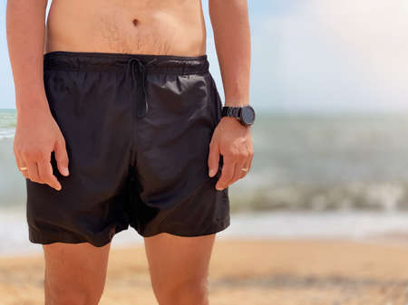 Close-up of a male torso in swimming black shorts on a beach against the background of the seaの写真素材