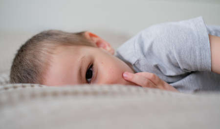 Close-up of a small happy caucasian boy in a gray t-shirt lies on the bed and smilesの写真素材