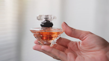 Perfume bottle in a female hand against the background of light room interior.の写真素材
