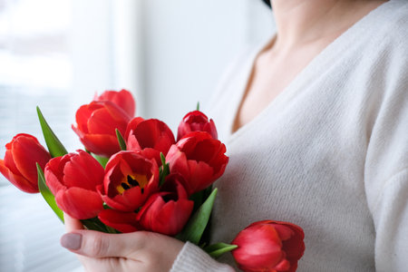 International Womens Day.Close-up of a woman in a white sweater with a bouquet of red tulipsの写真素材