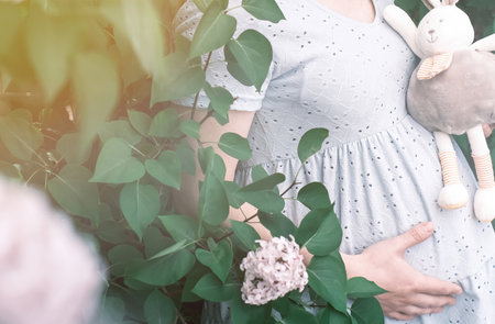 Close-up of a pregnant girl in a soft blue dress with a bouquet of white chrysanthemums and a toy bunnyの写真素材