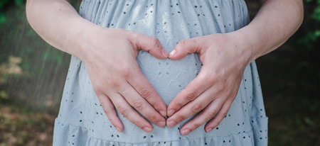 A pregnant woman is holding her belly in the shape of a heartの写真素材
