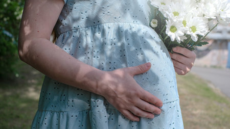 A pregnant woman is holding a bouquet of white flowers while wearing a blue dress