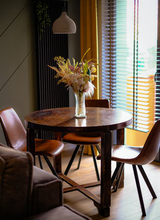 A table with four chairs and a vase of flowers in the center. The table is surrounded by a couch and a windowの写真素材