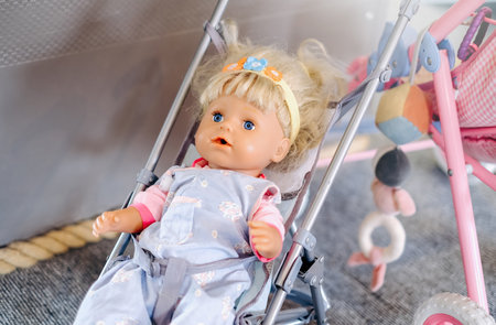 A doll is sitting in a stroller. The doll is wearing a yellow headbandの写真素材