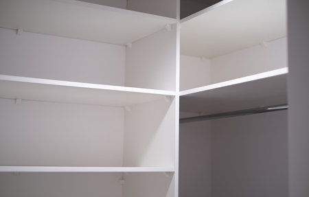 Minimalist white closet interior with clean, empty shelves and a clothing rod.の写真素材