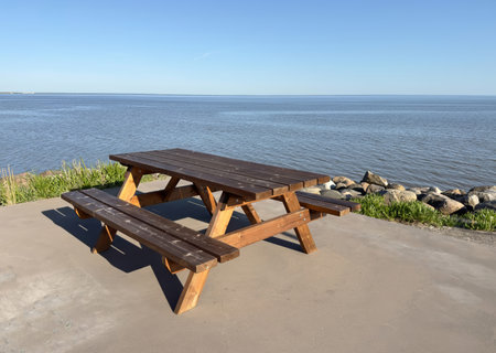 Wooden picnic table with benches placed on a concrete platform by the calm sea