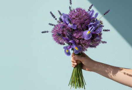 A hand holds a beautiful, elegant bouquet of fresh flowers against a bright, light blue backgroundの素材