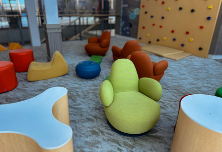A brightly lit, colorful indoor kids play area features modern, low-to-the-ground furniture, including orange, yellow, and green rounded chairsの写真素材