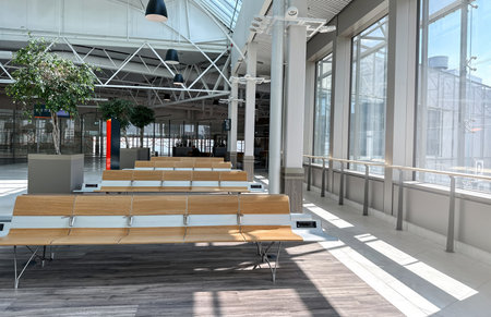 A wide-angle, contemporary interior view of a bright, empty waiting area within an airport, train...