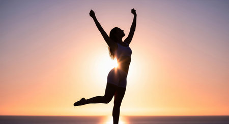 Silhouette of a fit, happy woman raising her arms against a beautiful sunrise or sunsetの素材