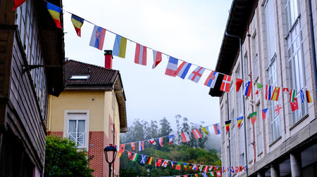 Festive street scene in Arriondas, Asturias, Spain, decorated with strings of colorful international flags hanging between buildingsの写真素材