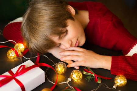 The boy sleeps next to a gift and a garland. Waiting for Santa, Christmas, and new yearの写真素材