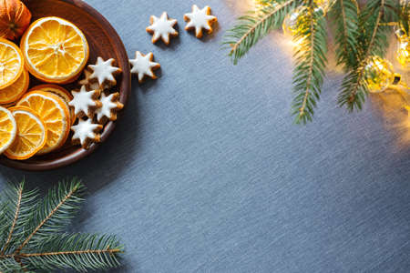 Winter background with dried oranges, ginger cookies pine tree branch and shiny garland on blue tablecloths. Top view, copy spaceの写真素材