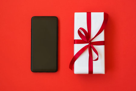 White gift box and a smartphone on red backgroundの写真素材