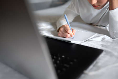 Close up of a person making notes in front of laptop