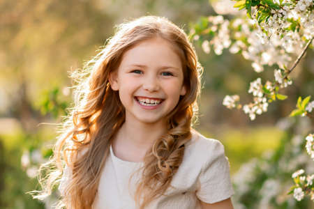 Portrait of happy girl in spring among white cherry blossom flowers.の写真素材