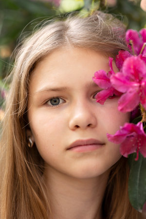 Portrait of young pretty teenage girl with flower near the face. Purple, magenta flowers blush. girl in spring garden.の写真素材