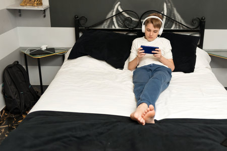 Teenager boy laying on the bed, playing games or watch videos, communicate on social media on mobile phone at homeの写真素材